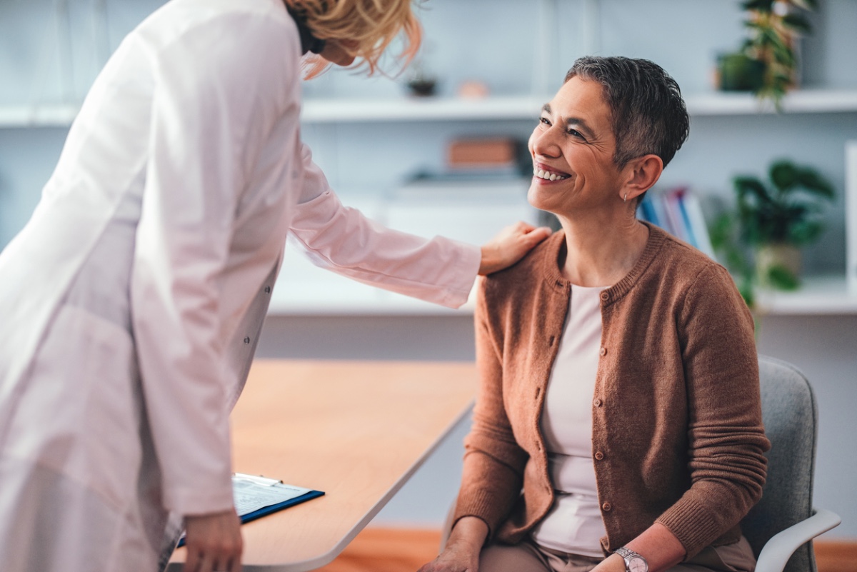 Doctor placing a reassuring hand on a smiling patient’s shoulder during a consultation
